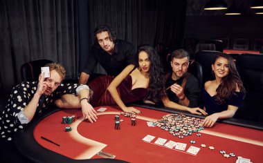Masaya uzanmış bir kadın. Kumarhanede birlikte poker oynayan bir grup zarif genç..