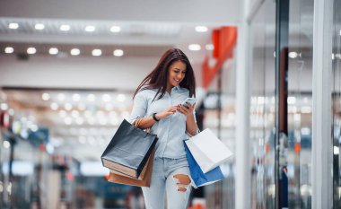 Süpermarkette elinde bir sürü paket ve telefonla esmer bir kadın alışveriş yapıyor..