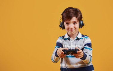 Stüdyoda sarı arka planda video oyunu oynayan sevimli küçük çocuk..