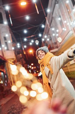 Sıcak kıyafetler içindeki mutlu genç çift Noel süslenmiş caddede beraberler..