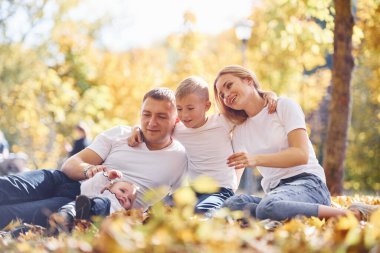 Neşeli genç bir aile yerde uzanıyor ve birlikte sonbahar parkında dinleniyorlar..