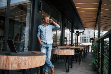 Telefonda sohbet ediyorduk. Gündüz vakti kafede duran kot pantolonlu adamın ön görüntüsü..