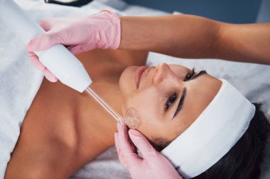 Kaplıca salonunda uzanan ve modern bir aletle yüz temizleme prosedürü uygulayan kadına yakından bakın..