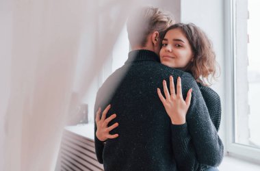 Pencerenin yanında birbirini kucaklayan sevimli genç bir çift..