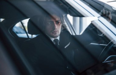 Siyah takım elbiseli ve kravatlı genç işadamı modern otomobil kullanıyor..