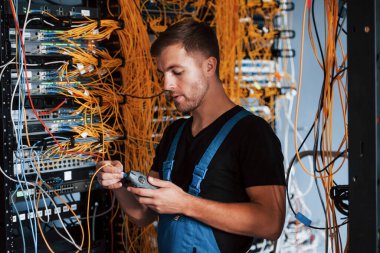 Ölçüm cihazlı üniformalı genç adam sunucu odasında internet ekipmanı ve kablolarla çalışıyor..