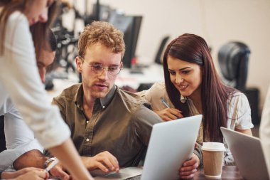 Masanın yanında oturuyor. Modern ofiste birlikte çalışan genç iş adamları..