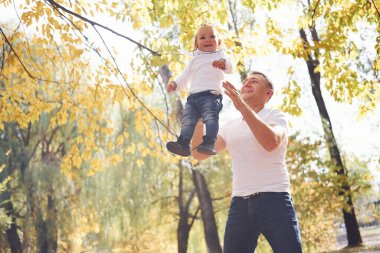Baba kızını elinde tutuyor ve sonbahar parkında eğleniyor..