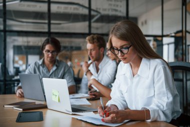 Sarışın kız belge okuyor. Ofiste çalışan resmi kıyafetli genç iş adamları..