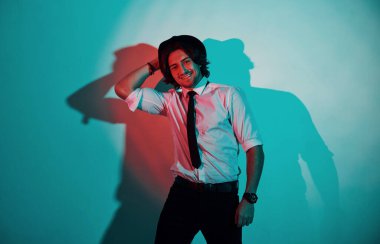 Stüdyoda neon ışıkları altında duran, resmi giyinmiş genç bir adamın portresi..