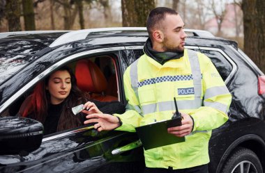 Yeşil üniformalı erkek polis memuru arabadaki kadından rüşvet alıyor..