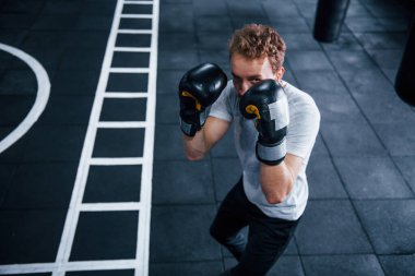Beyaz gömlekli ve boks eldivenli genç adam spor salonunda egzersiz yapıyor..