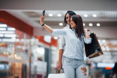 İki genç kadın süpermarkette alışveriş yapıyorlar ve selfie çekiyorlar..