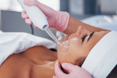 Kaplıca salonunda uzanan ve modern bir aletle yüz temizleme prosedürü uygulayan kadına yakından bakın..