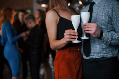 Partide arka plandaki arkadaşlara karşı birlikte duran içkili çiftin yakın görüntüsü.