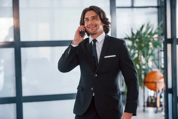 在办公室里通过电话交谈 穿着黑色西服打领带的年轻英俊商人的画像 — 图库照片