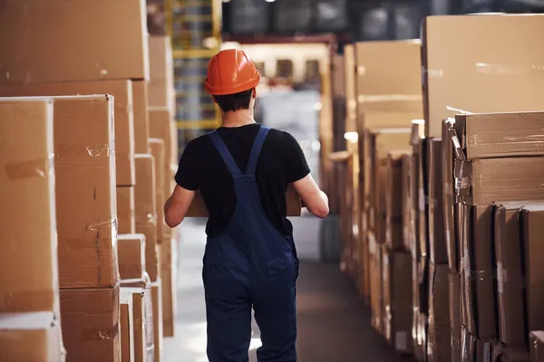 Joven Trabajador Almacenamiento Uniforme Sombrero Duro Lleva Caja Las Manos —  Fotos de Stock