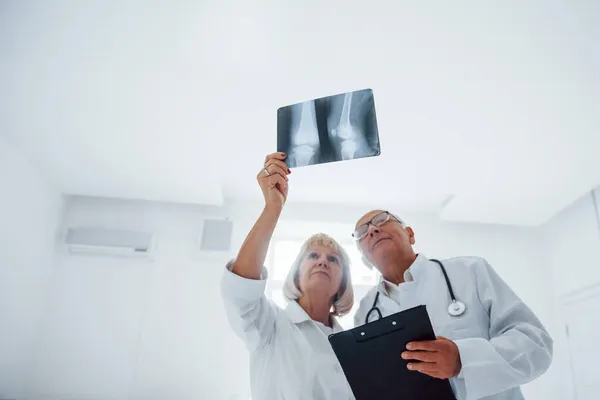Beyaz Üniformalı Kıdemli Erkek Kadın Doktorlar Insan Bacağının Röntgenini Inceliyor — Stok fotoğraf