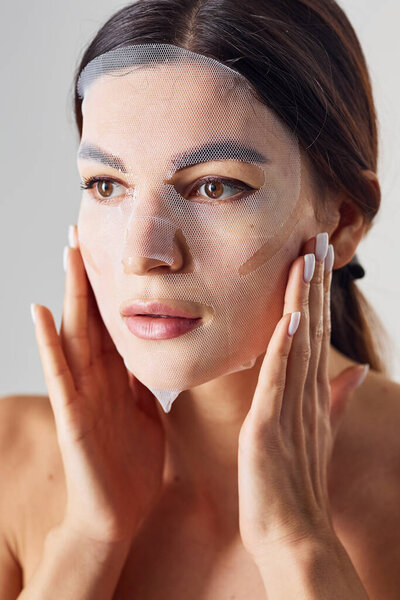 Портрет женщины в студии на белом фоне с маской красоты на лице.