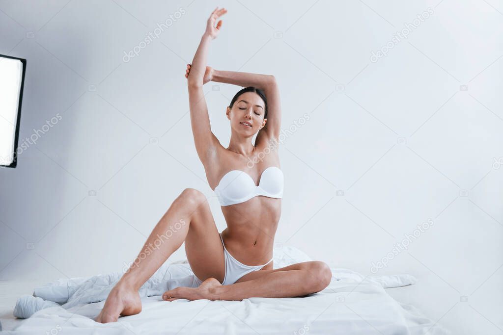 Young woman in underwear and with nice body shape sits in the studio against white background.