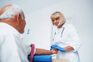 Kadın doktor klinikte yaşlı erkek hastaya iğne yapmaya hazırlanıyor..