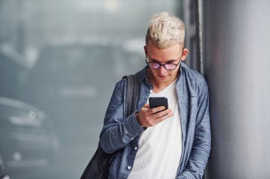 Güzel elbiseli hippi, gri arka planda, elinde telefonla içeride duruyor..