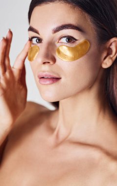 Çıplak kadın stüdyoda beyaz arka planda altın kasetlerle göz göze geliyor..