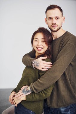 Stüdyoda birbirini kucaklayan gündelik giysiler içinde mutlu çoklu etnik çiftler. Asyalı kız arkadaşı olan beyaz bir adam..