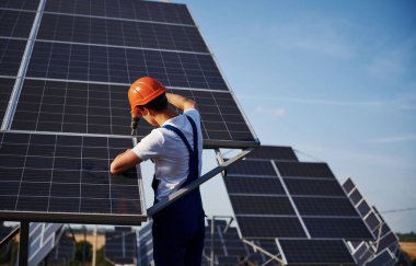Kablosuz tornavida kullanıyor. Açık havada mavi üniformalı, güneşli bir günde güneş pilli bir erkek işçi..