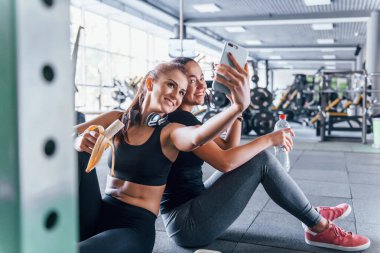Spor elbiseli iki bayan arkadaş spor salonunda meyvelerini topluyor ve selfie çekiyor..