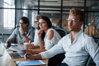 Gözlüklü sarışın adam çalışanların önünde. Ofiste çalışan resmi kıyafetli genç iş adamları..