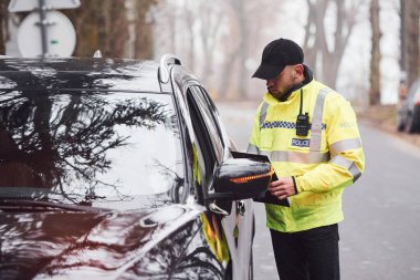 Yeşil üniformalı erkek polis yolda aracı kontrol ediyor..