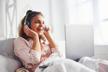 Kulaklık kullanarak müzik dinliyorsun. Hafta sonu vakti yatak odasında dizüstü bilgisayarla yatakta yatan tatlı bir kız..