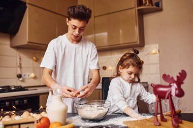 Erkek kardeşi ve kız kardeşi mutfakta un kullanarak yemek hazırlıyor ve eğleniyorlar..