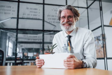 Aletlerle dolu bir kutu. Gri saçlı ve sakallı olgun iş adamı büroda..