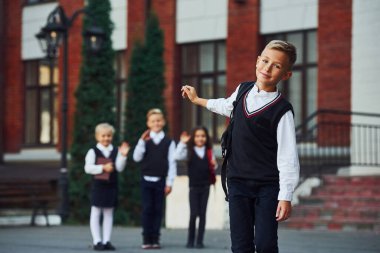 Okul üniformalı bir grup çocuk eğitim binasının yanında kameraya poz veriyor..