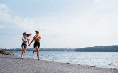 Güneşli bir günde göl kenarındaki sahilde koşup eğlenen iki bayan arkadaş..
