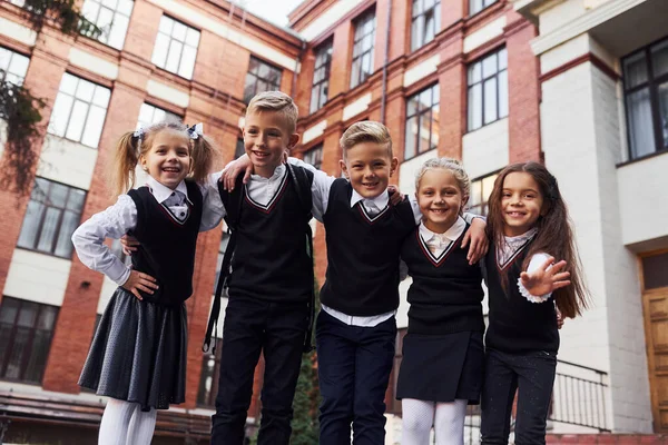 楽しさとお互いを受け入れること 学校の制服を着た子供たちが教育棟の近くで一緒に屋外にいます — ストック写真