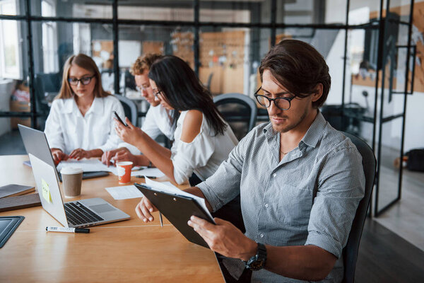 Guy in glasses in front of his employees. Young business people in formal clothes working in the office.