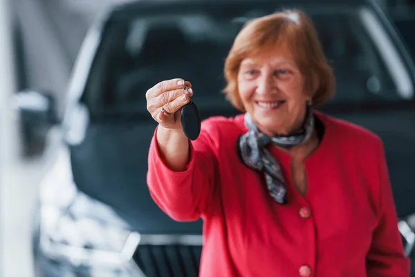 Happy aged woman in formal wear stands in front of modern white car.