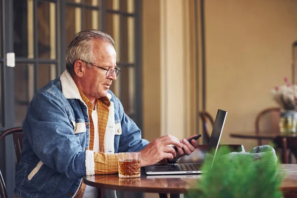 穿着时髦衣服和眼镜的时髦老年人坐在咖啡店里 与笔记本电脑一起工作 — 图库照片