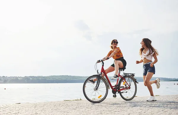 Girl runs near bicycle. Two female friends on the bike have fun at beach near the lake.