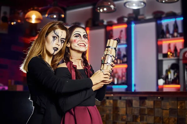 Two female friends is on the thematic halloween party in scary makeup and costumes with time bomb.