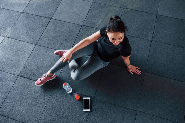 Top view of young woman in sportive clothes that sits on the floor with water in the gym.