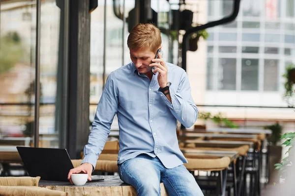 電話で会話してる 昼間に彼のラップトップで現代的なカフェにいる男のフロントビュー — ストック写真
