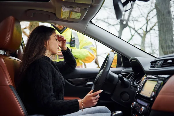 Girls feels bad. Male police officer in green uniform checking vehicle on the road.