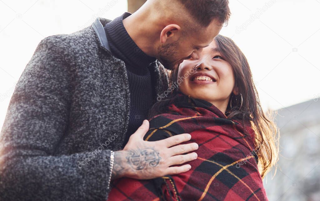 Happy multiracial couple warming up by red plaid together outdoors in the city.