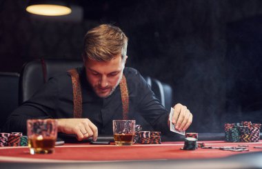 Zarif genç adam kumarhanede oturuyor, telefon kullanıyor ve poker oynuyor..