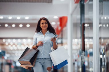 Süpermarkette elinde bir sürü paket ve telefonla esmer bir kadın alışveriş yapıyor..
