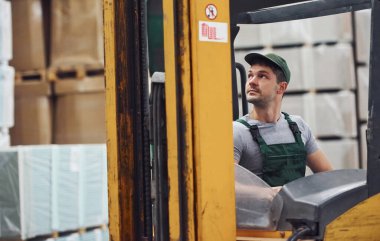 Üniformalı genç işçi depodaki forkliftte oturuyor..